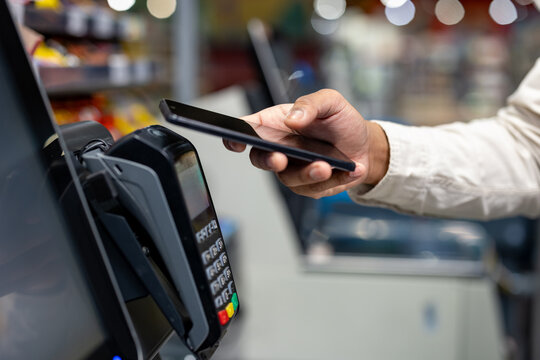 A person using a smartphone to make a contactless payment at a payment terminal in a store. It is a close-up shot. - Powered by Adobe