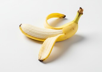 A single partially peeled banana with yellow skin and white flesh against a white surface in a studio shot