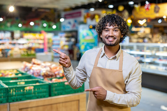 A smiling grocery store employee points to the fresh produce section, offering a friendly and inviting experience for customers in this environment.