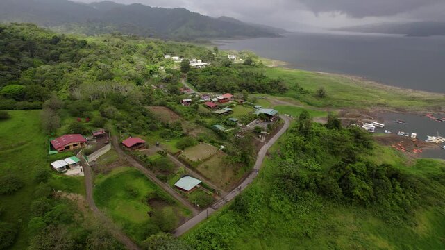 Aerial over El Fosforo lakeside town on Lake Arenal shore tilts up to stormy sky
