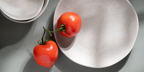 Flat lay of gray monochrome plates and tomatoes. Culinary concept with space for text
