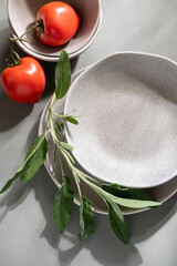 Flat lay of gray monochrome plates with tomatoes and sage. Culinary concept with space for text

