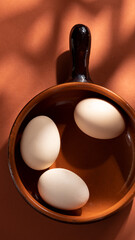 Handmade ceramic plates with home eggs on brown background. Terracotta objects, space for text. Genuine food concept.
