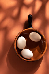 Handmade ceramic plates with home eggs on brown background. Terracotta objects, space for text. Genuine food concept.
