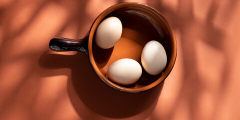 Handmade ceramic plates with home eggs on brown background. Terracotta objects, space for text. Genuine food concept.
