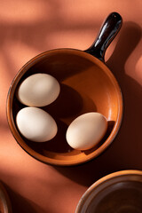 Handmade ceramic plates with home eggs on brown background. Terracotta objects, space for text. Genuine food concept.
