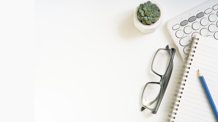 A white background with a plant, a pair of glasses, keyboard and a pencil. Isolated white background