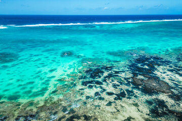 Breathtaking aerial view of the wave-swept coral reef off the coast of Mauritius, with beautiful seabed and black volcanic rocks in the foreground