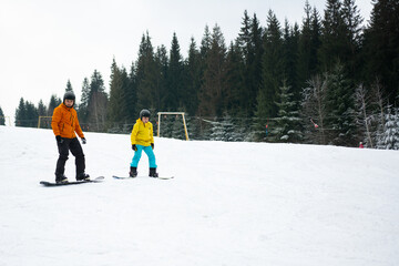 Winter adventure unfolds on a snowy slope as two snowboarders glide gracefully down the hill, surrounded by a tranquil forest of evergreen trees