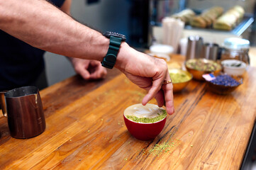 Barista adding pistachio topping to cappuccino in coffee shop