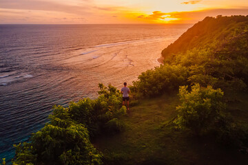 Man staying on ocean coastline with bright sunset in Bali. Drone view