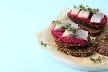 Tasty sandwiches with herring and horseradish sauce on light blue background, closeup. Space for text