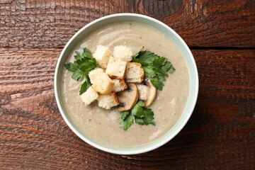 Delicious mushroom cream soup with croutons and parsley on wooden table, top view