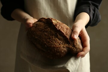 Woman with fresh loaf of bread on grey background, closeup