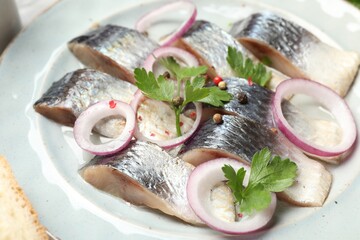 Pieces of delicious herring with spices and onions on table, closeup