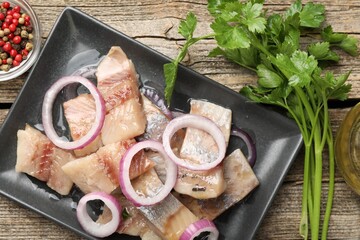 Pieces of herring with onions, peppercorns and parsley on wooden table, flat lay