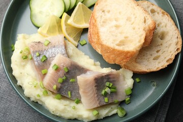 Pieces of delicious herring, mashed potato, cucumber slices and bread on black table, closeup