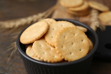 Tasty salty crackers and wheat spikes on wooden table, closeup