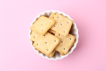 Tasty salty crackers on pink background, top view