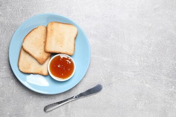 Slices of tasty toasted bread, jam and knife on grey textured table, flat lay. Space for text