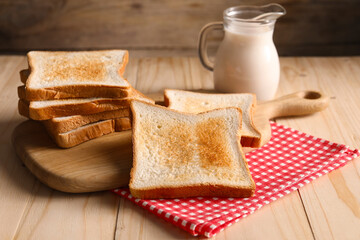 Slices of tasty toasted bread and jug of milk on wooden table, closeup