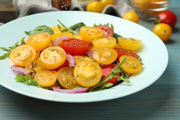 Fresh salad with yellow tomatoes on light blue wooden table, closeup