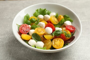 Tasty salad with yellow tomatoes, basil and mozzarella cheese on light grey table, closeup