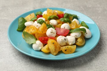 Tasty salad with yellow tomatoes, basil and mozzarella cheese on light grey table, closeup