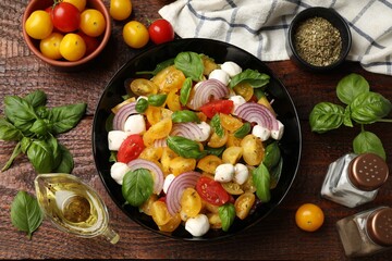 Tasty salad with yellow tomatoes, basil, onion and mozzarella cheese on wooden table, flat lay
