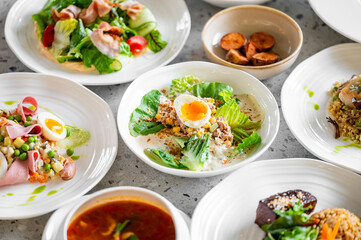 A selection of gourmet dishes on white plates, including fresh salads, boiled eggs, roasted...