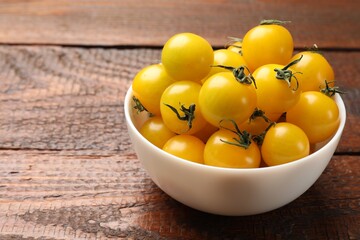 Many fresh yellow tomatoes in bowl on wooden table, closeup. Space for text