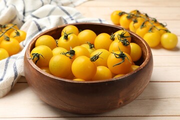 Many fresh yellow tomatoes in bowl on light wooden table, closeup