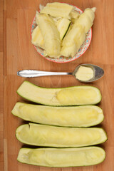 Halved and scooped-out zucchinis are arranged with removed pulp in a bowl and on a spoon on a wooden board