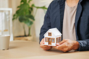Close-up of a real estate agent hand holding a small house model, symbolizing property, home loan,...