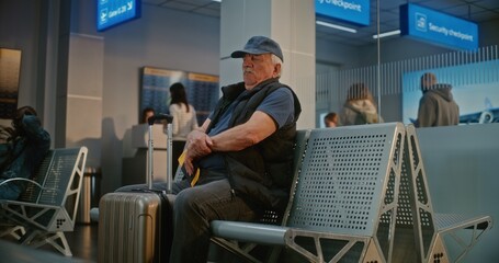 Crowded Airport Terminal: Senior Man with Suitcase and Passport Sitting in Departure Hall After...