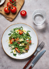 Healthy arugula salad with cherry tomatoes, mozzarella and pesto sauce on a light background