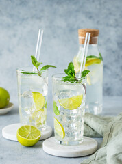 Two glasses and bottle mojito cocktail with fresh lime, mint and ice on a marble stand on blue texture background.