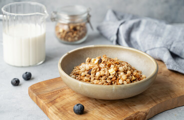 Homemade baked granola or muesli in a bowl on a wooden board on a light background