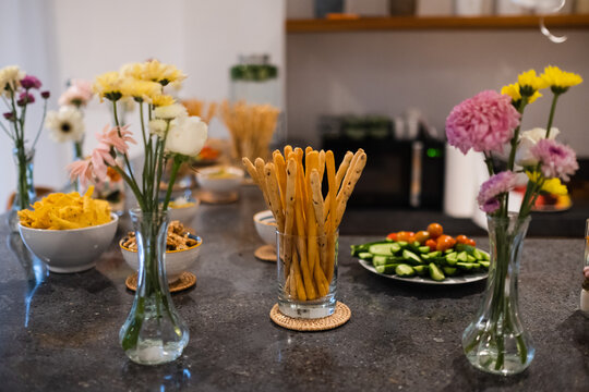 Healthy snacks and breadsticks with fresh vegetables on kitchen table, cozy home food setup.