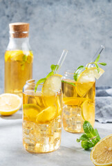 Two glasses and bottle with iced drink with lemon and mint on a light background
