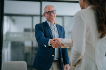 Senior businessman and businesswoman shaking hands in a modern office, both smiling and expressing happiness after successfully closing a deal or signing an important contract