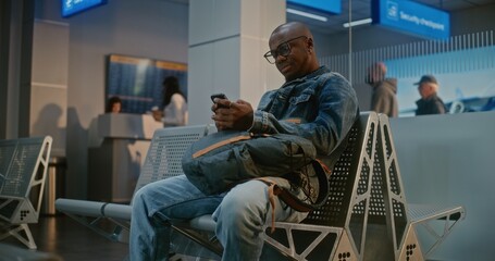 International Airport Terminal: African American Man with Backpack Sitting in Boarding Lounge After...