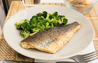 Fried fillet of sea bass with garnish of broccoli on black warm stone plate