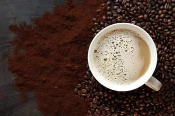 Cappuccino, top view. Cup of cappuccino among coffee beans and ground coffee. Cup of aromatic coffee among roasted coffee beans. Invigorating drink. Copy space