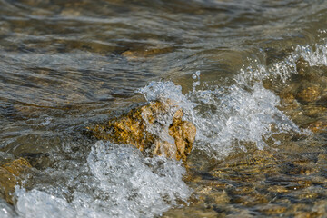 De petites vagues du lac Léman viennent doucement se briser sur un rocher en bord de rive, créant des éclaboussures légères et une atmosphère paisible au bord de l’eau.