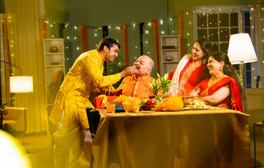Looking at camera, cheerful Indian family eats laddoo or laddu at home on festive Diwali evening