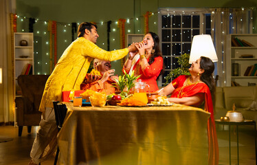 Looking at camera, cheerful Indian family eats laddoo or laddu at home on festive Diwali evening