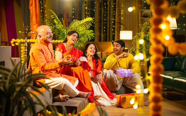 Joyful Indian family enjoying Diwali celebration together indoors with laddus, lights, and laught