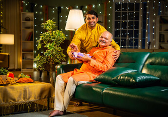 Surprising father with Diwali gift while sitting indoors with traditional festival home decorations