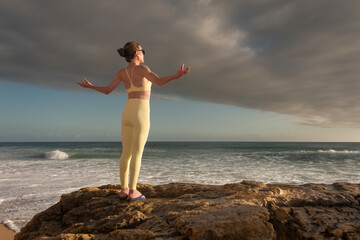 Fit sporty woman with her arms outstretched looking out at the ocean with dramatic sky
